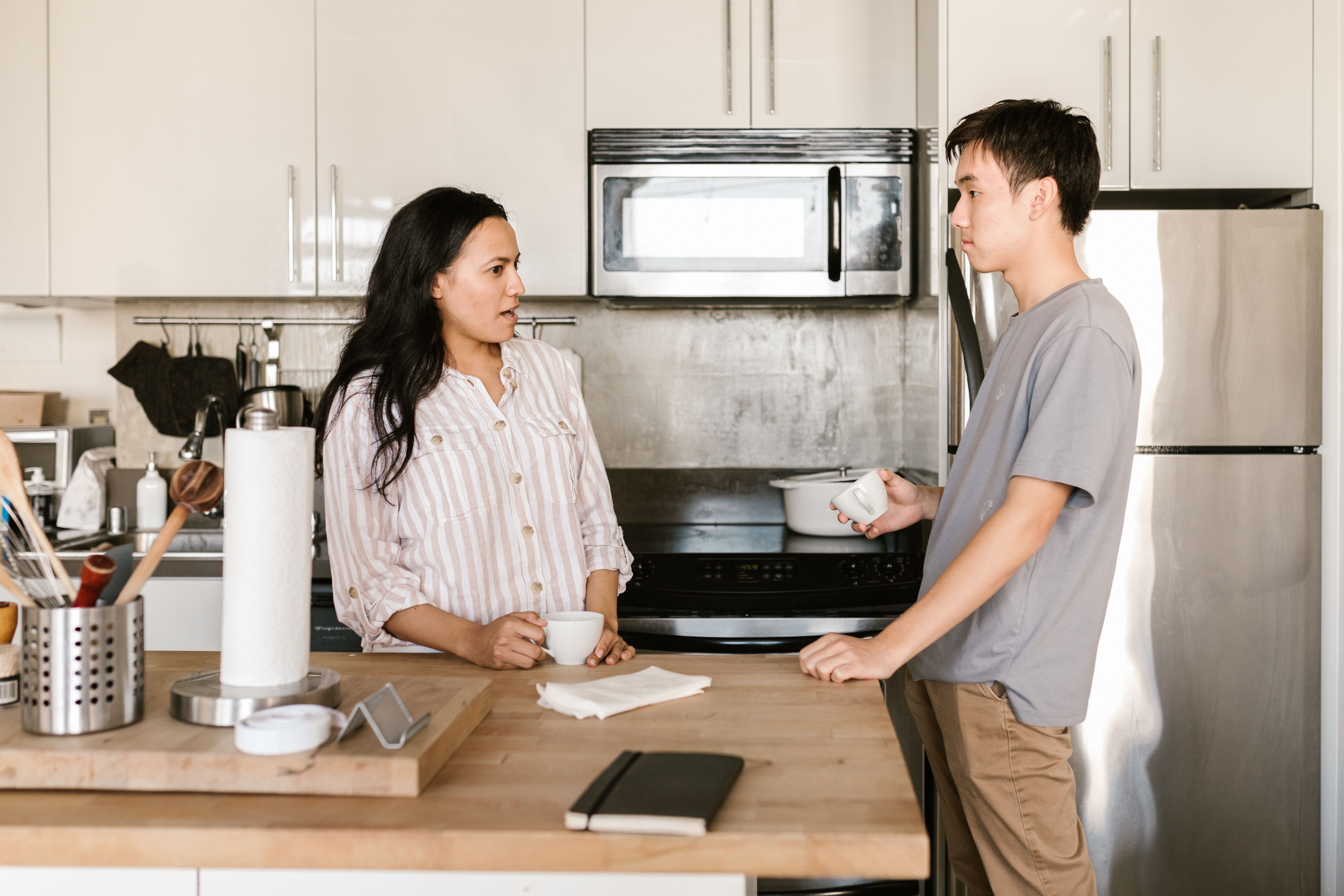 A parent and teenager talking over coffee in a kitchen