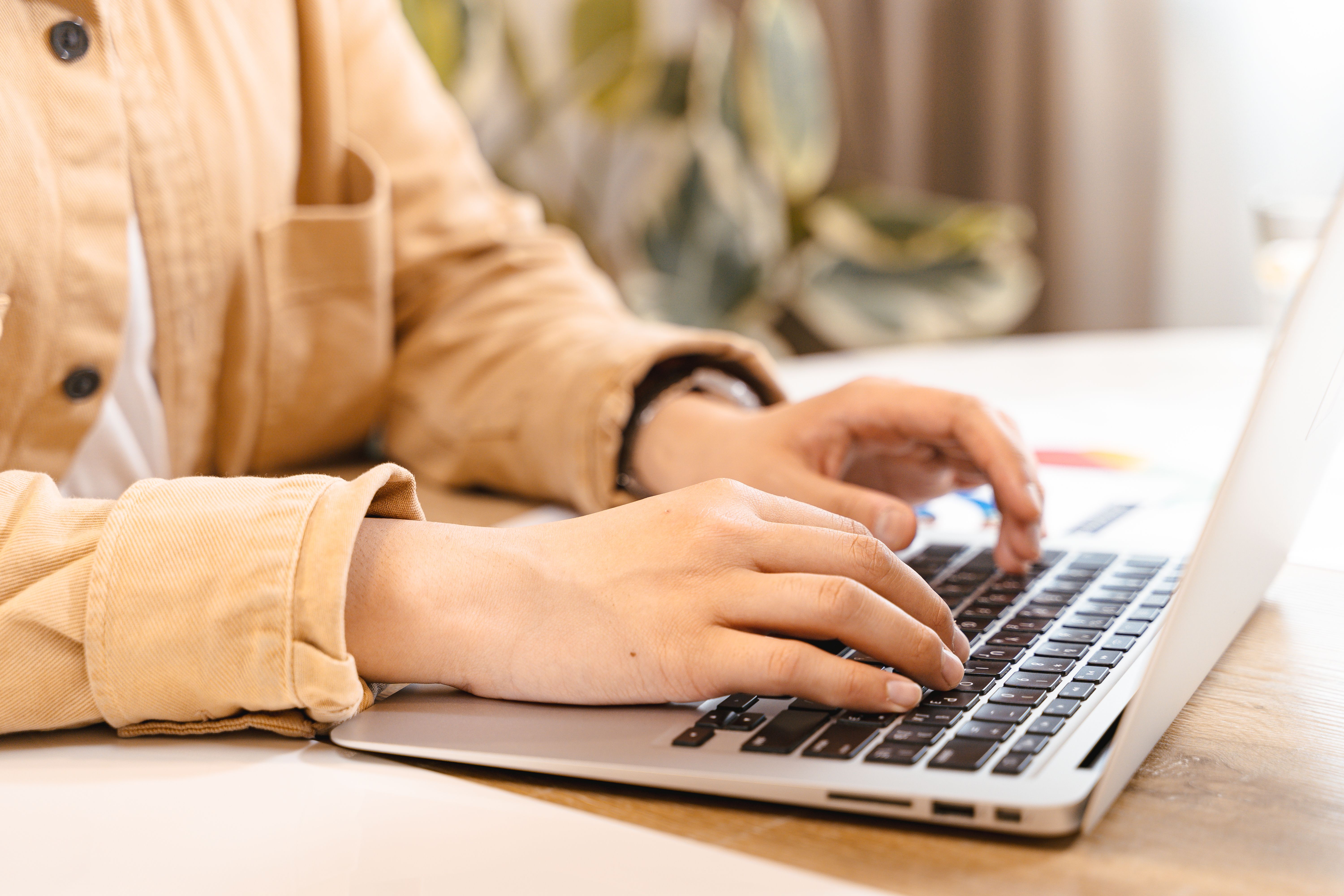 A person typing at a laptop while sorting paperwork