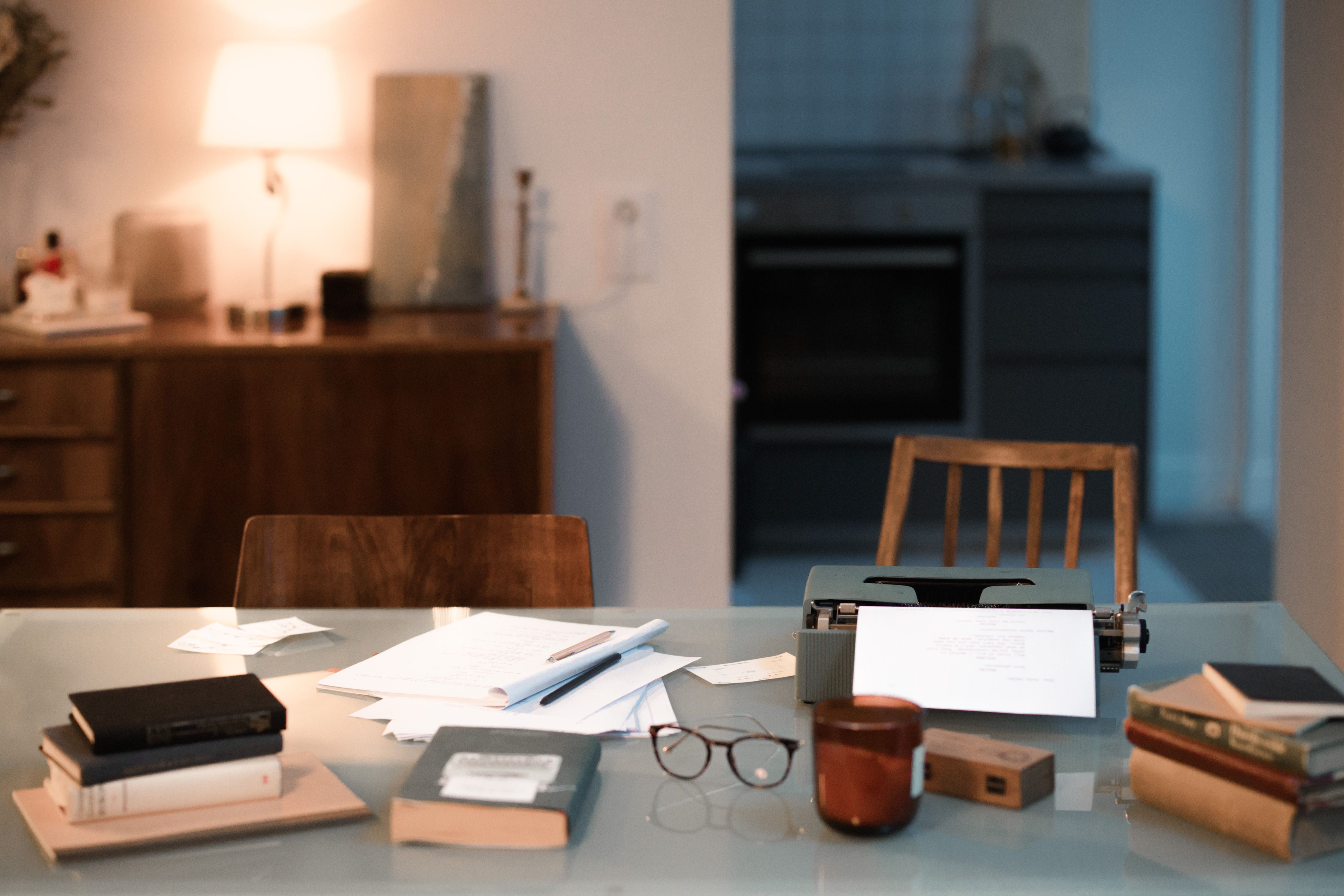 A kitchen table with paperwork, glasses and a candle in warm morning light